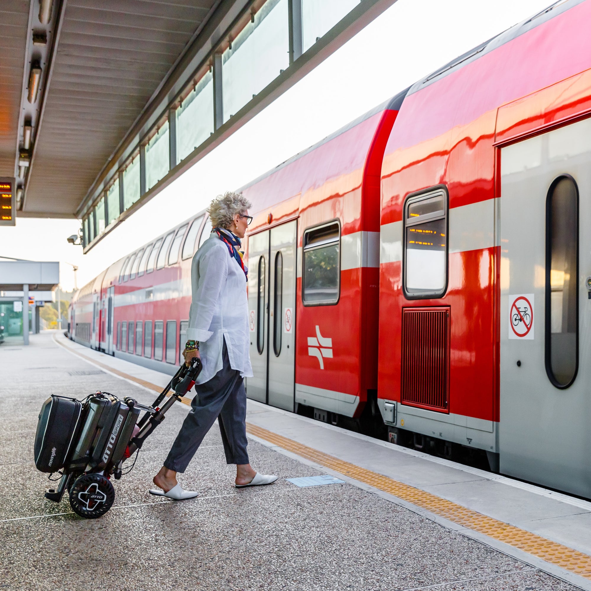 Woman traveling with the ATTO foldable mobility scooter in trolley mode. 