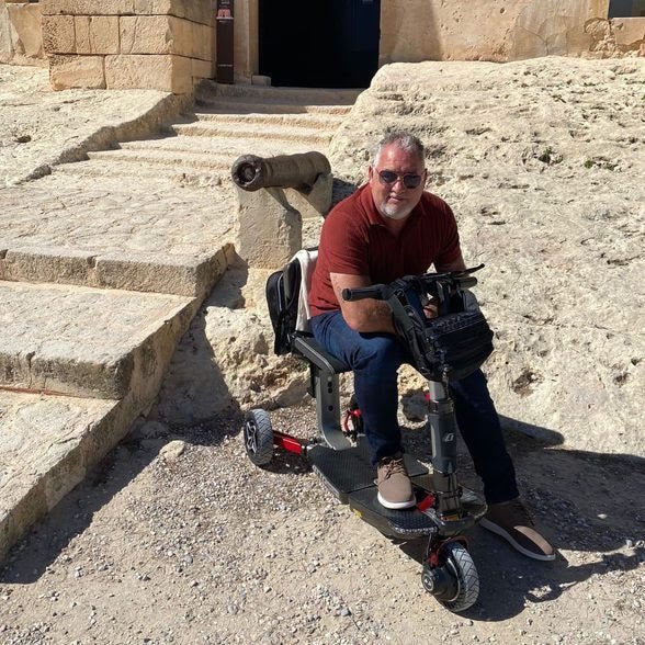 ATTO folding mobility scooter parked outdoors on a rural path, showcasing its compact design